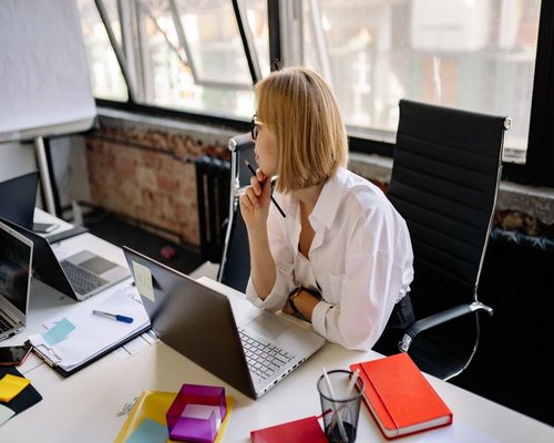 A professional woman working calmly in a shared office space in Guadalajara, taking a brief pause looking away from the monitor